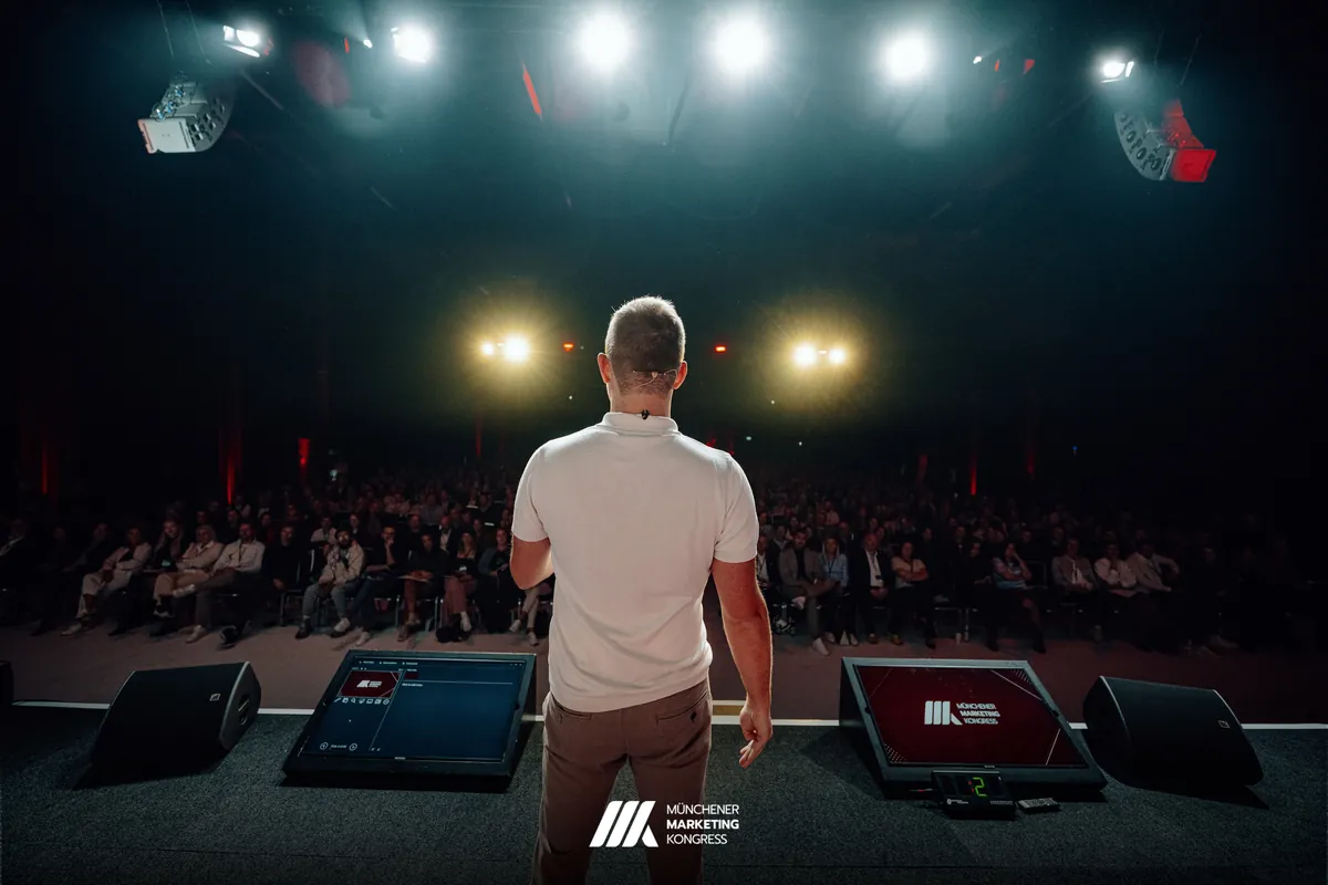 Marco Heer von hinten, vor ihm der volle Saal im Scheinwerferlicht